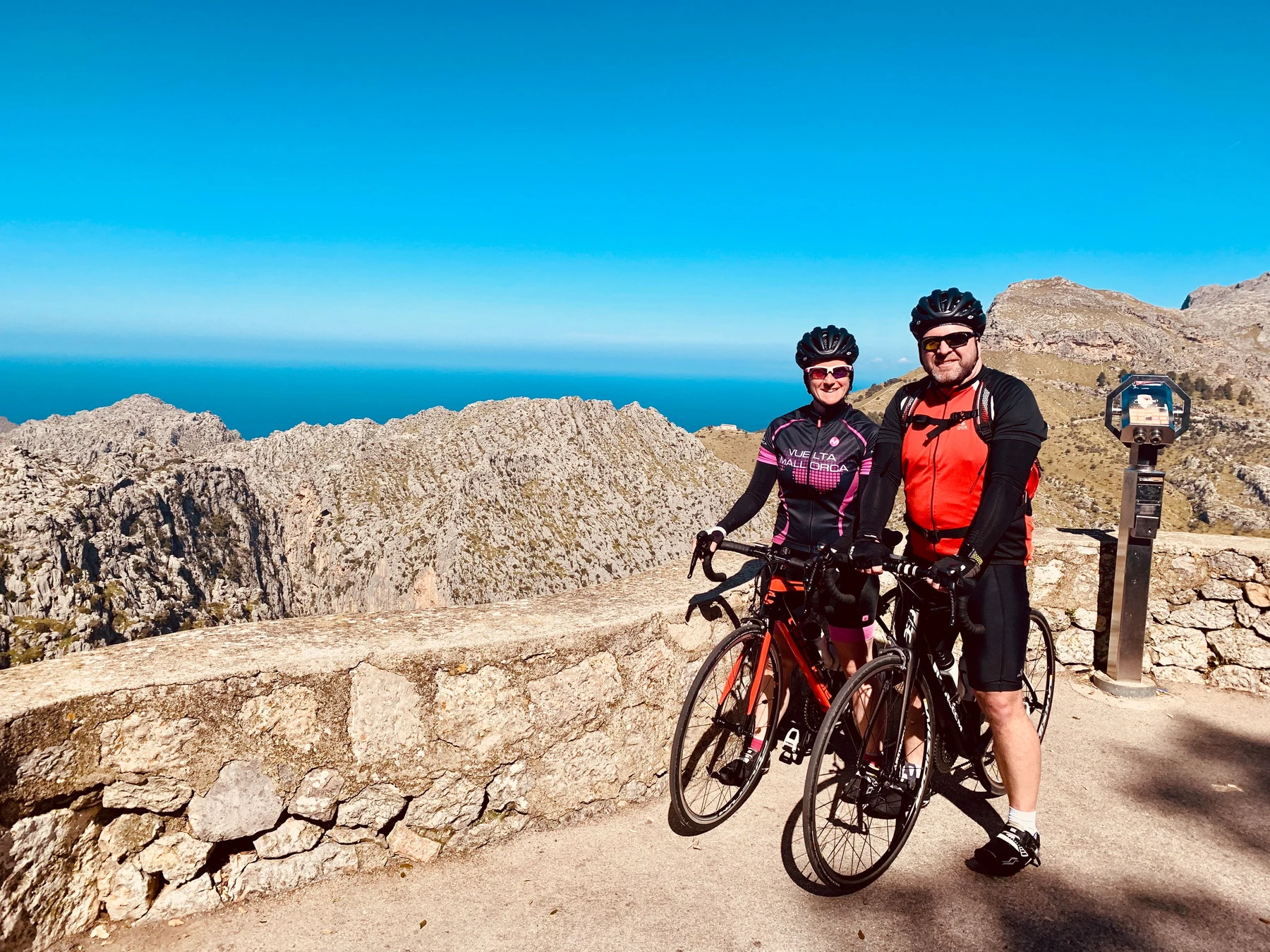 Anja und Rainer mit ihren Rennrädern an einer steinernen Mauer über dem Meer