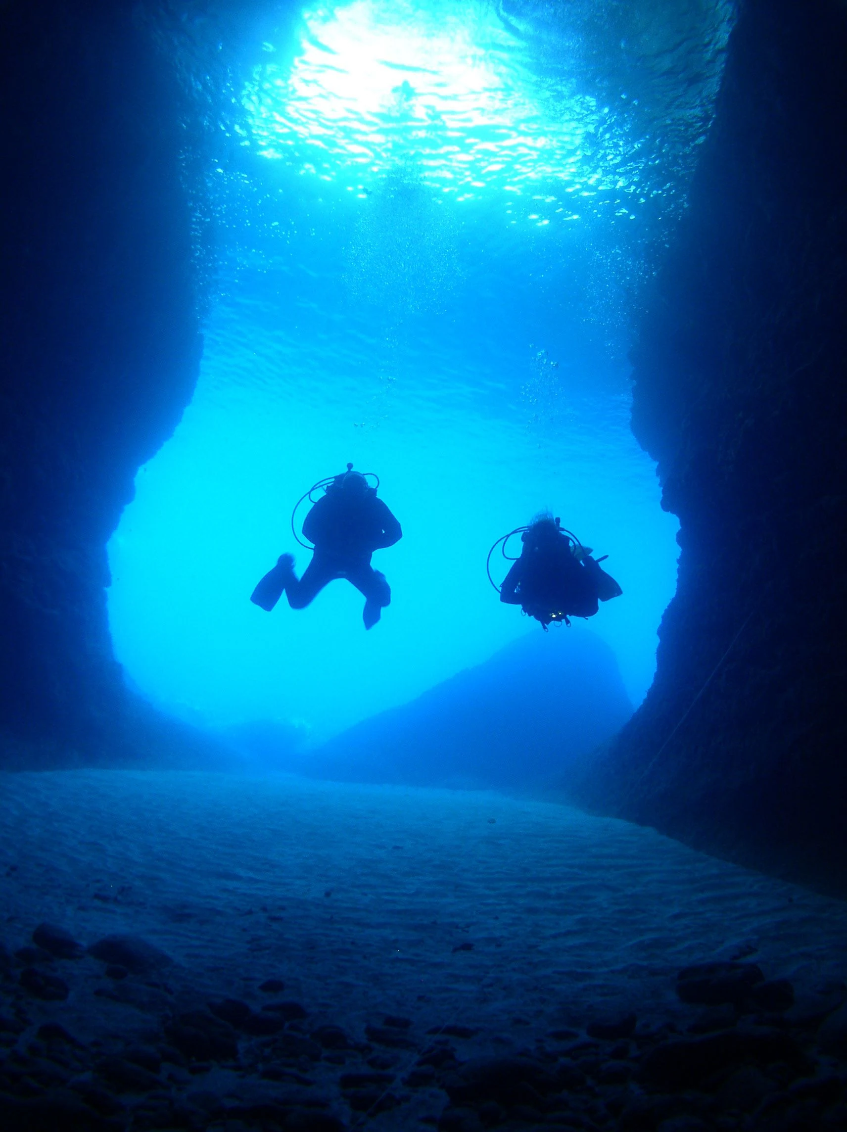Zwei Taucher als Silhouetten in einer tiefblauen Unterwasserhöhle